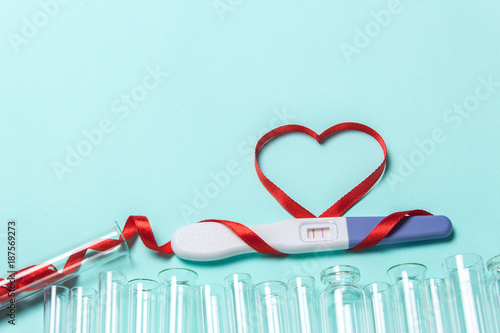 Artificial insemination, a child from a test tube, infertility treatment. Positive pregnancy test with two strips and a red ribbon in the form of a heart and a test-tube