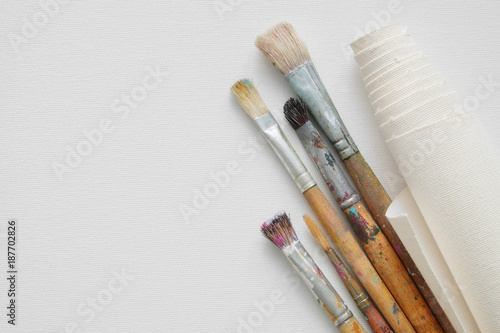 Paintbrushes and roll of artist canvas on white canvas background. Top view. Copy space for text.