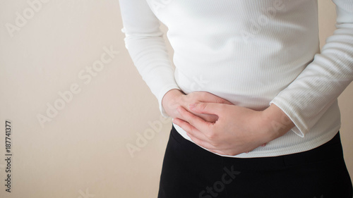 Young female suffering form abdominal pain on gray background w/ copy space. Causes of abdominal pain include dysmenorrhea, endometriosis, PMS or ovarian cyst. Gynecology and health care concept.