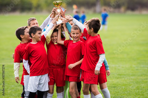 Kids soccer football - children players celebrating with a trophy after match on soccer field