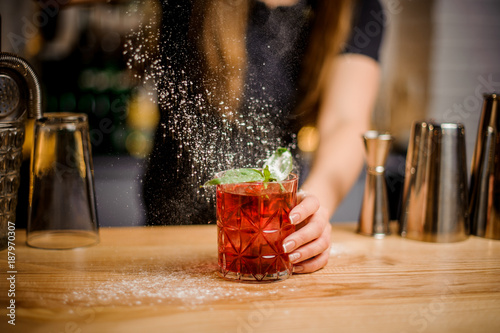 blondy barmaid finishes preparation of cocktail by adding a bitter of powdered sugar