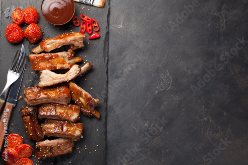 Pork ribs in barbecue sauce and honey roasted tomatoes on a black slate dish. A great snack to beer on a dark stone background. Top view with copy space