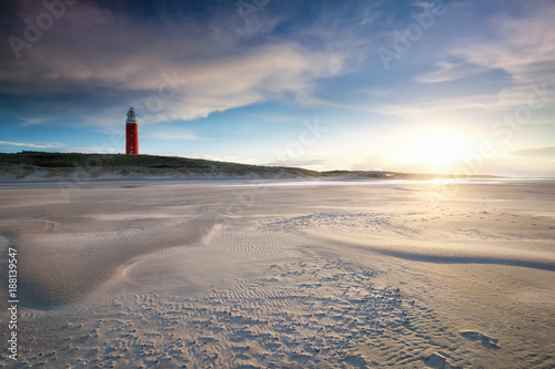 sunset behind red lighthouse on sea coast