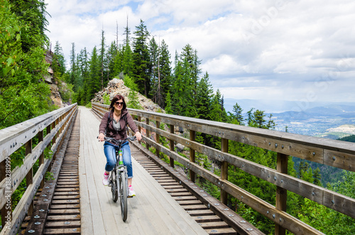 Woman Riding a Bicycle across a Wooden Bridge along a Mountain Path on a Spring Day.