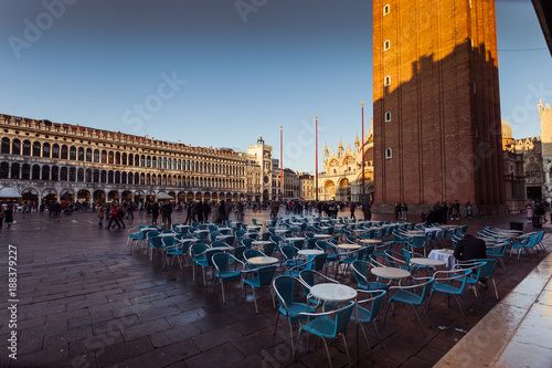VENICE, ITALY - JANUARY 02 2018: Florian Cafe small tables in San Marco square with cathedral and bell tower shadow at evening time. Florian is an historic venetian cafe