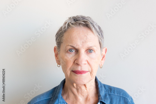 Portrait of beautiful older woman with short grey hair and striking blue eyes against neutral background (selective focus)