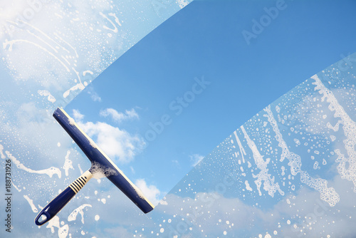 Rubber squeegee cleans a soaped window and clears a stripe of blue sky with clouds, concept for tranparency or spring cleaning, copy space in the background