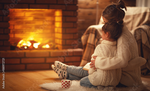 family mother and child hugs and warm on winter evening by fireplace.