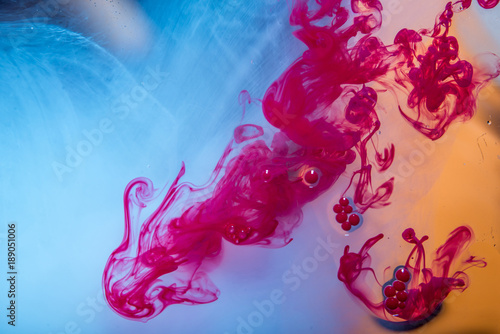 Swirls of red paint moving in the water like smoke on a blue background. Abstract background