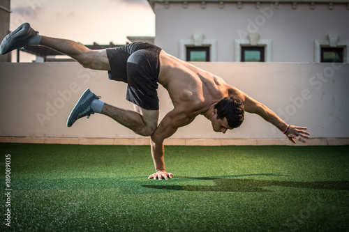 Young athletic man balancing while doing a one hand push up and holding his body in the air outdoors.