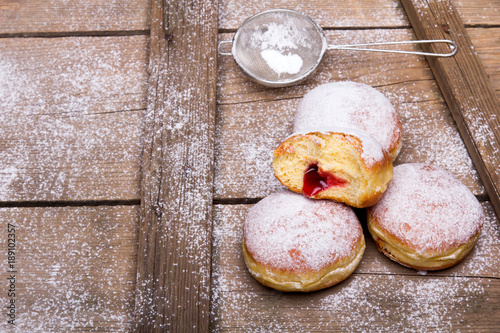 Tradycyjne pączki z cukrem pudrem i dżemem na drewnianym tle. Miejsce na tekst. 