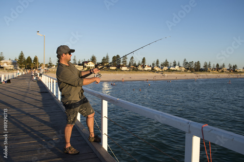 young attractive and happy man in shirt and hat fishing at beach sea dock using fish road enjoying weekend hobby in holidays