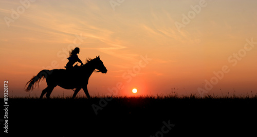 Horseback woman riding on galloping horse with red rising sun on horizon. Beautiful colorful sunset background with equine and girls silhouette horse hiking