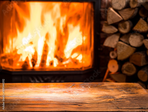 Old wooden table and fireplace with warm fire at the background.