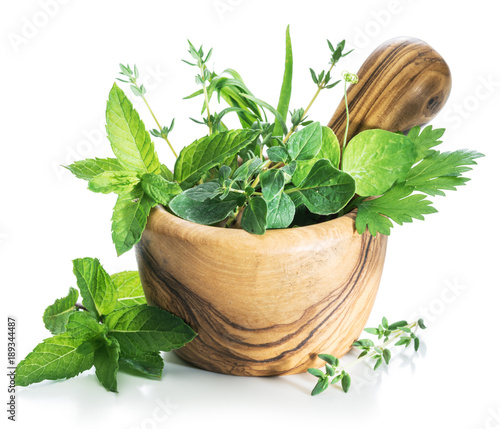 Different fresh green herbs in the wooden mortar.