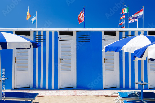 Colorful beach huts on summer day with blue sky. Flags on background.