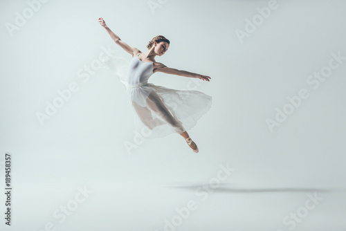 elegant ballet dancer in white dress jumping in studio, isolated on white