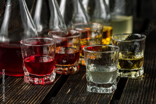 Assorted alcoholic cordials in glasses and decanters on dark wood background