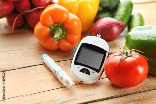 Digital glucometer, lancet pen and vegetables on wooden background. Diabetes diet