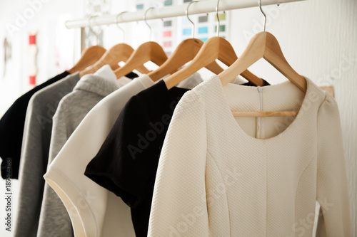 Women dresses new collection of stylish clothes wear hanging on hangers clothing rack rails, fabric samples at background, fashion design studio store concept, dressmaking tailoring sewing workshop