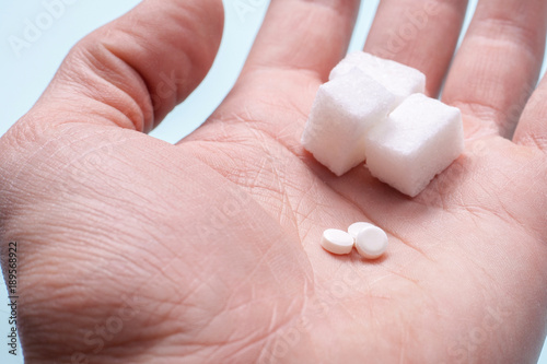 Choice of Sweetener in tablets or regular sugar. Alternative to sugar for diabetics. A man holds sugar and sugar substitute in his hand