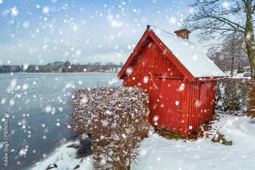 Snowy winter scenery with red wooden house at the lake in Sweden