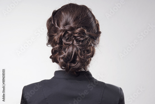 head of woman with brown hair in bun on gray isolated background rear view