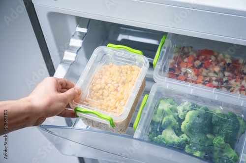 Woman taking container with frozen corn from refrigerator