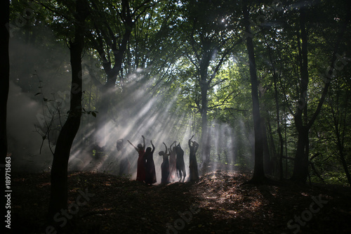 silhouette of a group of women in a dark forest with smoke