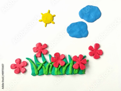 Colorful plasticine clay dough made are red flowers grass sun and clouds on white background, beautiful nature