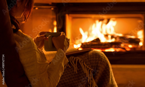 Young woman sitting at home by the fireplace and reading a book.