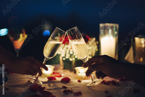 Romantic candlelight dinner table setup for couple with beautiful light as background. Man & Woman hold glass of Champaign. Concept for valentine's day and date.