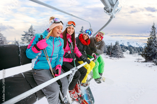 cheerful friends on ski lift ride up on snowy mountain