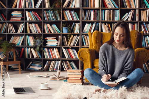 Young woman writer in library at home creative occupation sitting writing notes