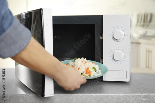 Woman putting plate of rice with vegetables in microwave oven, closeup