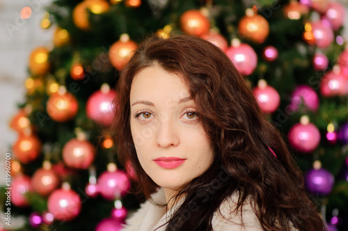 Attractive Brunette with Sensual Lips and Curly Hair is Posing in Studio with Christmas Decoration Looking at the Camera.