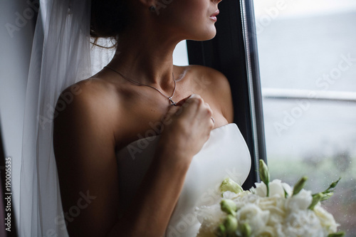 Girl in a white dress with a beautiful silver chain around her neck The bride fixes a decoration of a jewel on the neck Stylish fashionable diamond suspension the bride fixes the cross on the neck