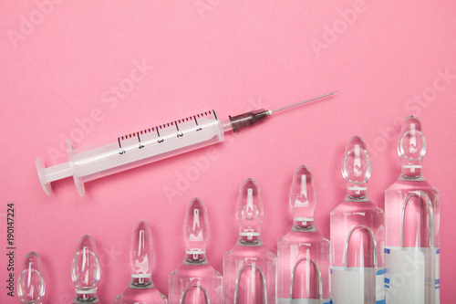 Increasing dependence on injections of hyaluronic acid, botox and collagen. Syringe and ampoules on a pink background.