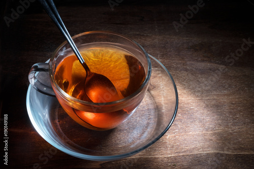 black tea freshly brewed in a glass cup and a spoon on a dark rustic wooden table, steaming hot drink against cold and flu, creative lightning, copy space