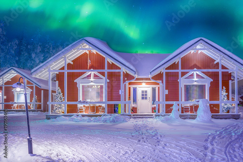 Travel Destinations Concepts. Beautiful Multicoloured Vibrant Aurora Borealis known as Northern Lights Playing with Vivid Colors Over Traditional Lapland Houses in Finland.