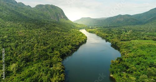 Aerial view of river in tropical green forest with mountains in background