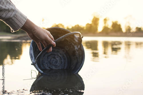 Close-up hand of woman holding a bucket on lake, crisis of water and drought