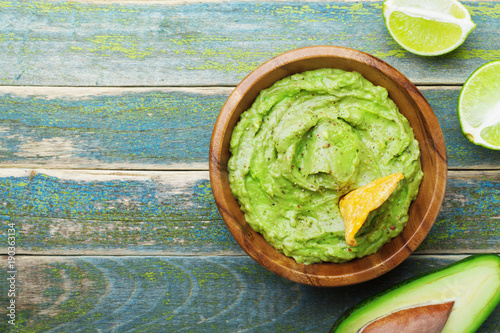 Green guacamole with ingredients avocado, lime and nachos on wooden vintage table top view. Traditional mexican food.