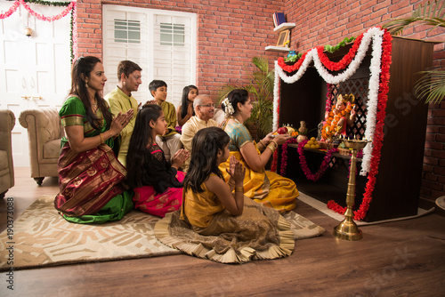 Indian family performing Ganesh puja or Ganpati Puja in Ganesh Utsav, or holding ganesh idol over white background 