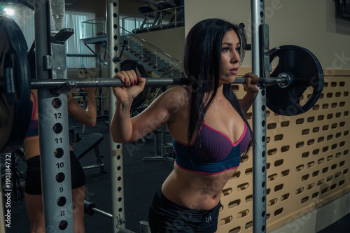 Portrait of beautiful brunette is holding a barbell in the gym. Close-up
