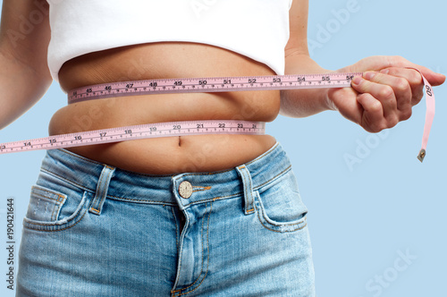 Overweight woman with tape measure around waist on pastel background