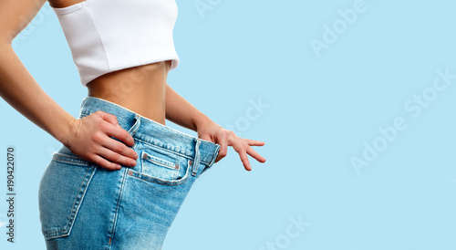 Weight loss. Woman in oversize jeans on pastel blue background