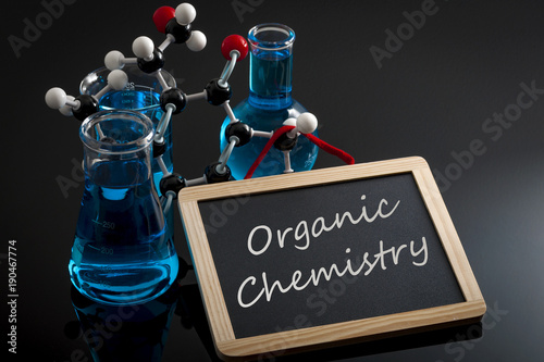 Chemical reaction, science class and STEM concept with a model of a molecule on chemistry glassware and flasks filled with blue liquid and a chalkboard with organic chemistry written on