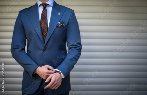 Male model in tailored suit posing outdoors and fixing his cufflinks