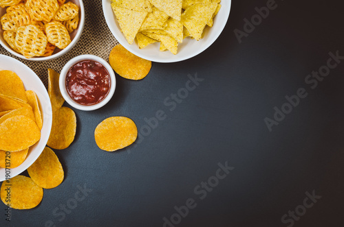 Party snacks - potato chips and snacks in bowl on black slate table. Photograph taken from above, top view with copy space around products.